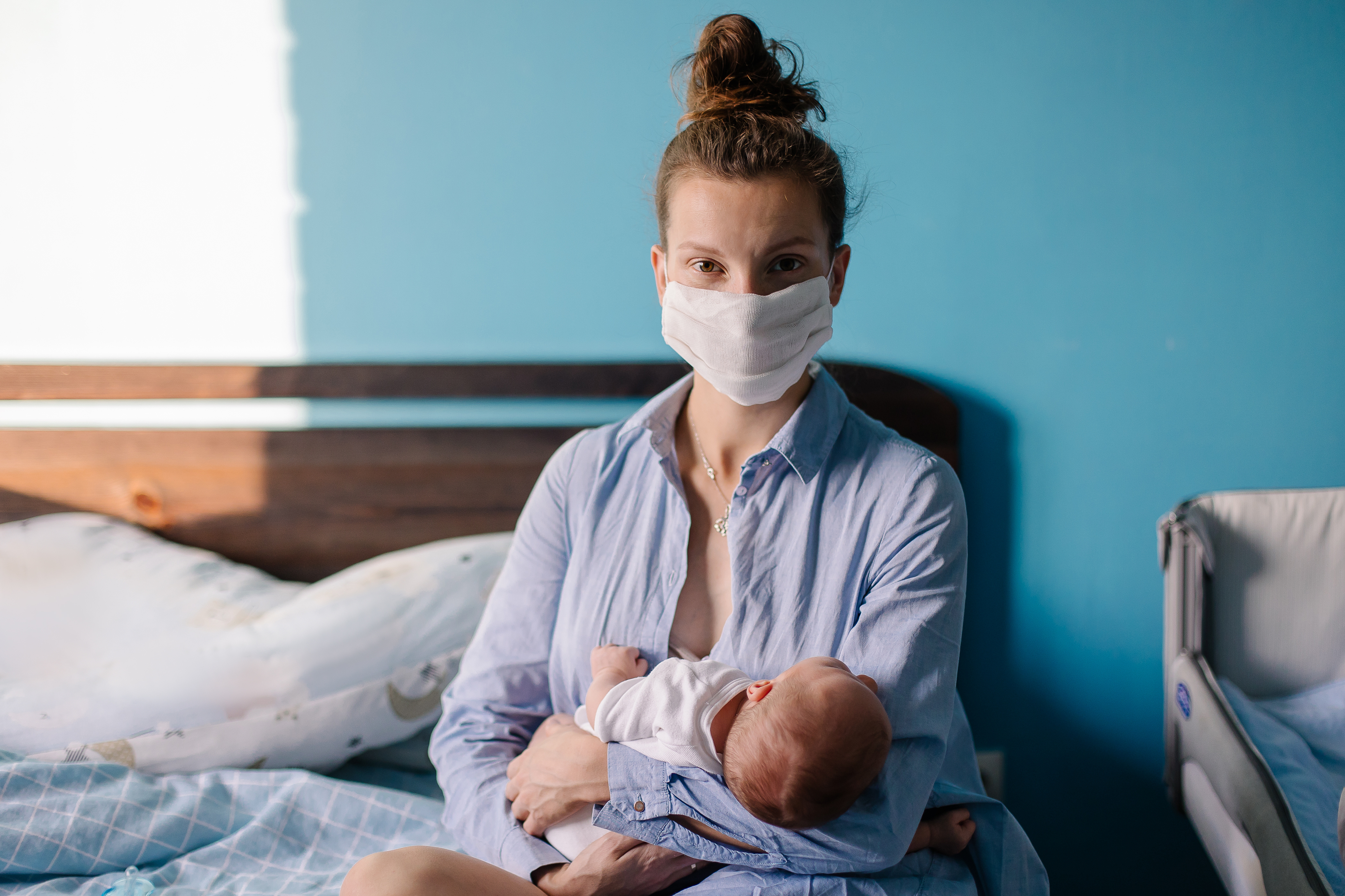 New parent holding newborn wearing a face mask