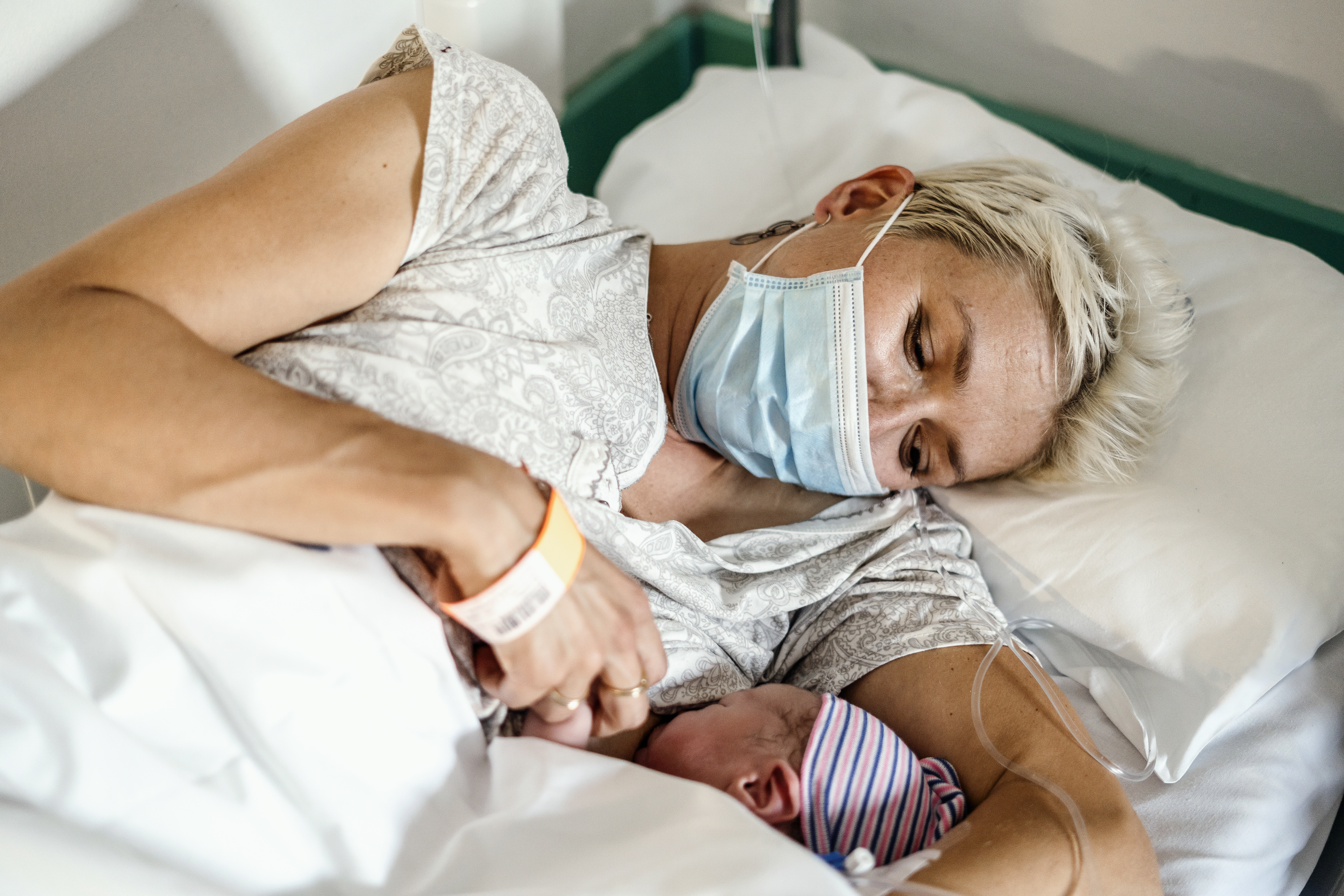 New parent body feeding their newborn while wearing a face mask in the hospital