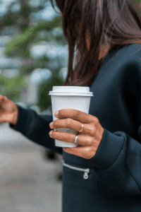 woman with long, brown hair is holding a takeaway cup of coffee