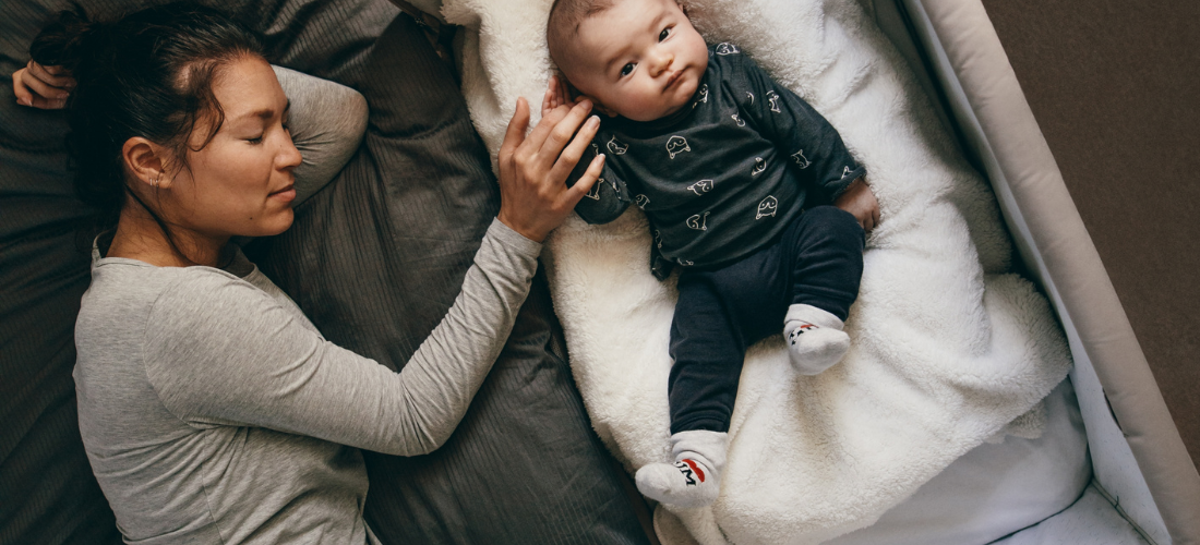 New mother comforting her newborn baby while lying in bed and baby is in bassinet