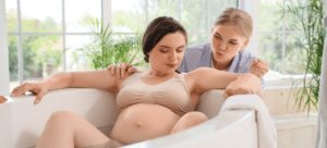 Pregnant woman in labour, is in a bathtub. Doula is behind her coaching with breathing techniques.