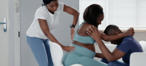 Doula massages the birthing parent's back, while the birthing parent leans on her partner for emotional support