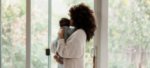 New mom holding her newborn while looking away in front of a sliding door