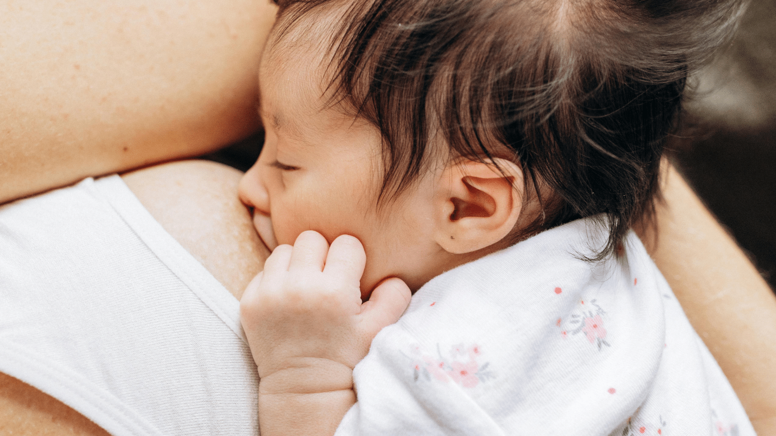 Baby breastfeeding while being held close to their mother, demonstrating the breastfeeding support postpartum doulas help families achieve.